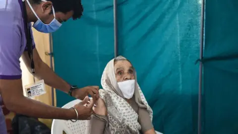 AFP/Getty Images A health worker gives an elderly woman a Covid-19 vaccine at the Tagore Hall in Ahmedabad on 18 March 2021