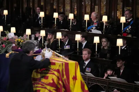 PA Media (front row, left to right) The Duke of Sussex, Princess Charlotte, the Princess of Wales, Prince George, watch as the Imperial State Crown and the Sovereign's orb and sceptre are removed from the coffin of Queen Elizabeth II, draped in the Royal Standard, during the Committal Service at St George's Chapel in Windsor Castle, Berkshire