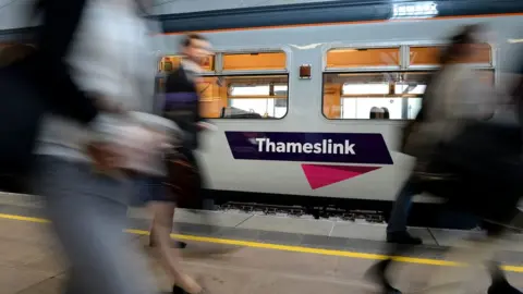 PA Media Passengers walking past a Thameslink train