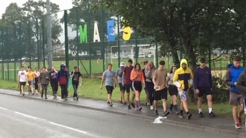 A group of young people walking by a sign for Maes B