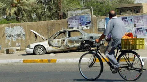 AFP An Iraqi man rides a bicycle past the remains of a car burnt during a deadly incident involving Blackwater guards in Baghdad in September 2007