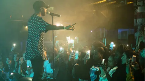 Ben Dance 6lack stands in front of a crowd of young apprentices who are recording the show on their phones