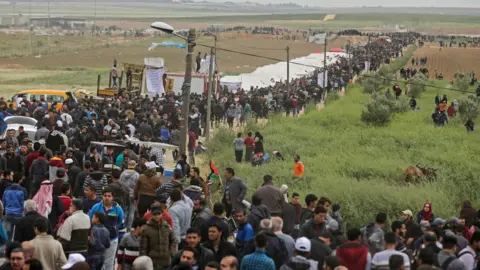 AFP Palestinians march past a tent city erected along the border with Israel east of Gaza City. 30 March 2018