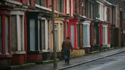 Getty Images Man walking beside derelict homes