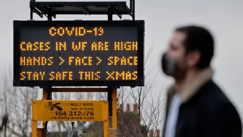 Getty Images A man walks past a sign warning of high Covid cases