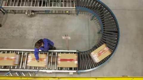 Getty Images/Alistair Berg Worker scanning boxes on a conveyor belt