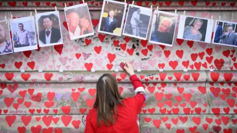 Getty Images Woman writes on Covid memorial wall in London