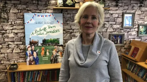 BBC Image of Hannah Dosanjh. A poster of "A Railway Town Called Swindon" can be seen next to her.