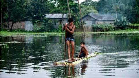 Getty Images Indian children paddle a raft through floodwaters