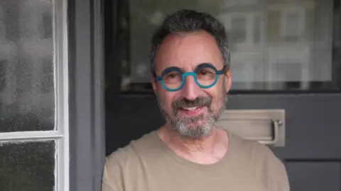 Image of Julian Futter wearing round green glasses, standing in his doorway