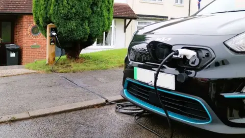 charger plugged into front of black car outside house