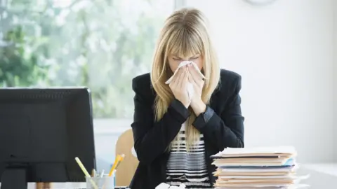 Getty Images A women blows her nose in work