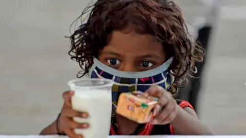 Getty Images A poor child takes a glass of milk and a packet of biscuits during a free glass of milk and biscuit packet distribution organised by Kolkata police amid coronavirus emergency in Kolkata, India, 23 May, 2021. In