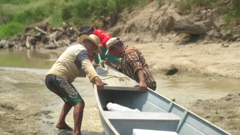 Paul Harris / BBC Oliveira and friends tugging his canoe along the dried-out creek