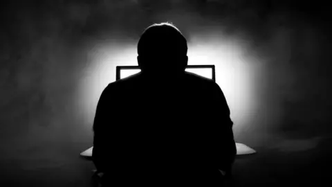 Getty Images silhouette of man sat in front of computer