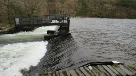 Geograph / Malc McDonald Water flows out of Crummock Water over a weir, into the River Cocker.