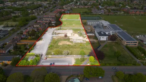 Eddisons Commercial Limited, Cambridge An aerial view of a school which has large playing fields either side. On the left, a playing field and car park is outlined with a red line. There are hundreds of homes around the school site.
