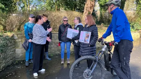 Olivia Richwald/BBC Seven people stand around in a circle, including Smith's daughters, who are holding signs around their necks.
