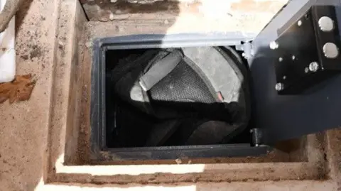 Greater Manchester Police A hole in the pavement floor of a shed where a grey safe has been uncovered containing a rucksack  