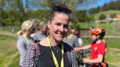 A woman with hair tied on her back and sunglasses on her head smiling at the camera. She was wearing a black top.