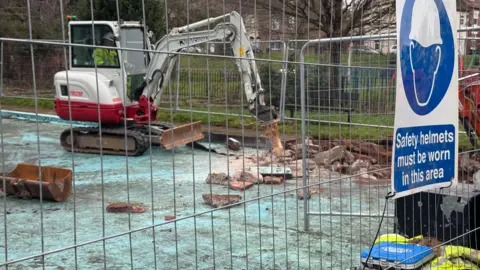 A digger starts to demolish a concrete base on a derelict swimming pool. 