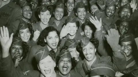 US Army A black and white image showing a packed group least 20 women in  US World War Two uniform smiling and waving towards the camera in about 1946