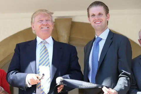 Getty Images Donald Trump and Eric in smart suits and ties holding a ribbon and pen smiling at the camera on a sunny day