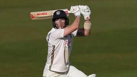 Right-hander Matthew Potts with the bat above his head as he plays a shot through the offside in evening sunshine in Durham