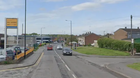 General view of Mill Street in Armthorpe, with a garage on the left-hand side, houses on the right and cars driving along the road.
