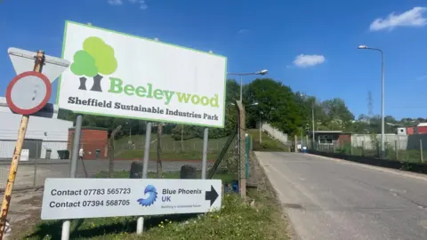 A large white sign with bright green writing at the edge of a road entrance