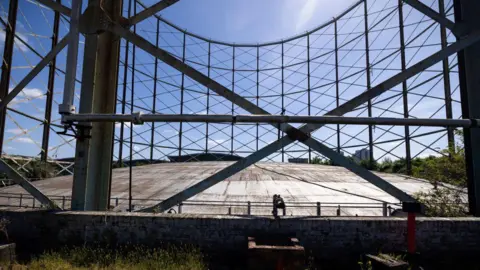 Getty Images Steel framework of a disused circular gasholder seen from inside, with criss-crossing metal beams and open sky above, highlighting the scale and structure of the historic industrial site.