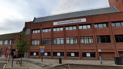 A red brick building with at least three floors is pictured with a large rectangle-shaped sign that reads Marks and Spencer.