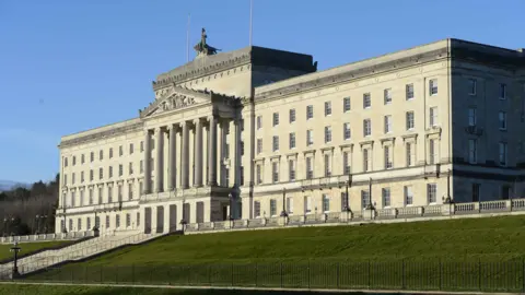 Getty Images A large white stone building sits on a green grass bank. White steps with black hand rails can be seen in front of the building.