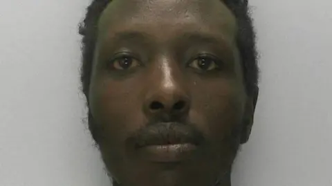 A bearded man looking at the camera in a police mugshot
