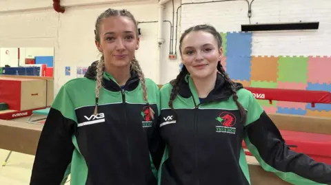 Mia Rowley and Nel Thomas in Ynys Mon Island Games jackets standing in front of aparatus