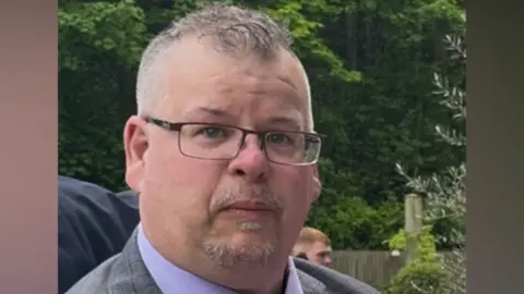 Local Democracy Reporting Service A headshot of Craig Wiles. He is wearing glass and looking at the camera. He has short grey hair and a grey goatee. He is standing outdoors. In the background there are a number of trees.