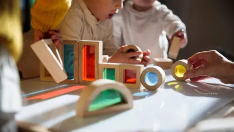 Two boys sat at table with rainbow shapes on their school desk to play with. You can only see their hands and the top of their chest.