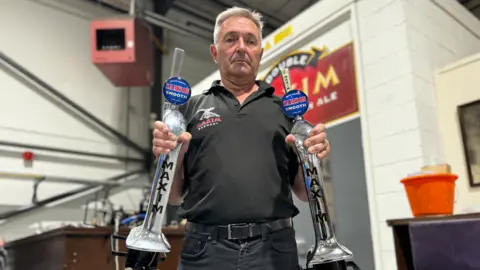 A man stands holding two beer pumps removed from a bar