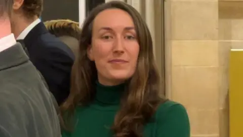 Councillor Heather Mack, looking into the camera. She has long brown hair and is wearing a green top.