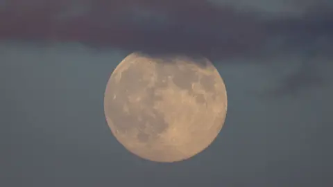 Getty A full moon, partially covered by dark cloud, shining with a yellow tinge