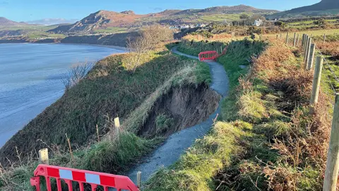 Barriers prevent people walking along a path where "chunk" has disappeared due to a landslip