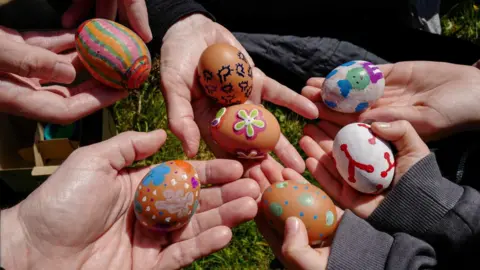 Getty Images A group of people's hands are holding out eggs that have been decorated and painted. 