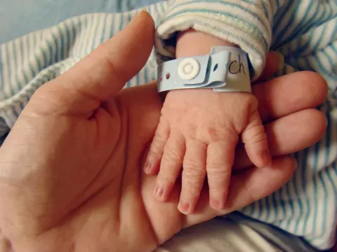 Getty Images Newborn baby's hand, with a hospital identification wristband round it, being held by their mother