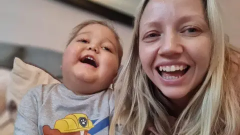 Supplied Karen and Max sat smiling and looking directly at the camera.