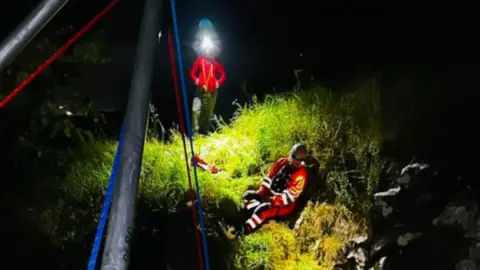 Derbyshire Cave Rescue Organisation Two volunteers in high vis and with torches on, in the dark, with a grassy area lit up