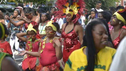 Getty Images Niños y mujeres vestidos con coloridos disfraces de carnaval, con tocados amarillos y rojos, bailan en un desfile.