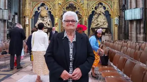 Margaret Peacock Margaret Peacock at King Charles' coronation in 2022.  She has short white hair and glasses and is wearing a long black coat over a black and white blouse.