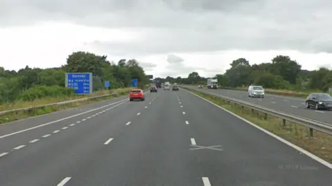 Google maps street view of the M4 westbound carriageway near junction 17 for Chippenham, Wiltshire. Multiple cars can be seen travelling on both carriageways and the end of the slip road can be seen at the side of the frame. A blue road sign indicating where the nearest service stations are is on the left of the roadside. 