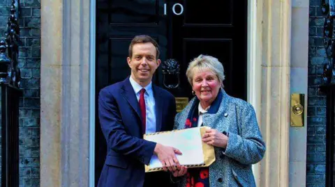 77-year-old Maltby resident Shirley Carruthers and Rother Valley MP Jake Richards holding the petition in a brown envelope in front of the door to 10 Downing Street.