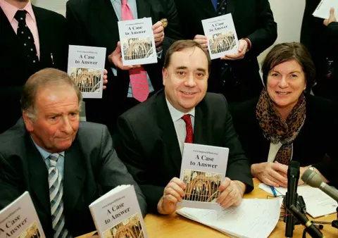 Getty Images Alex Salmond surrounded by a radical  of different   MPs holding up   copies of a publication  making the lawsuit  for the impeachment of Tony Blair